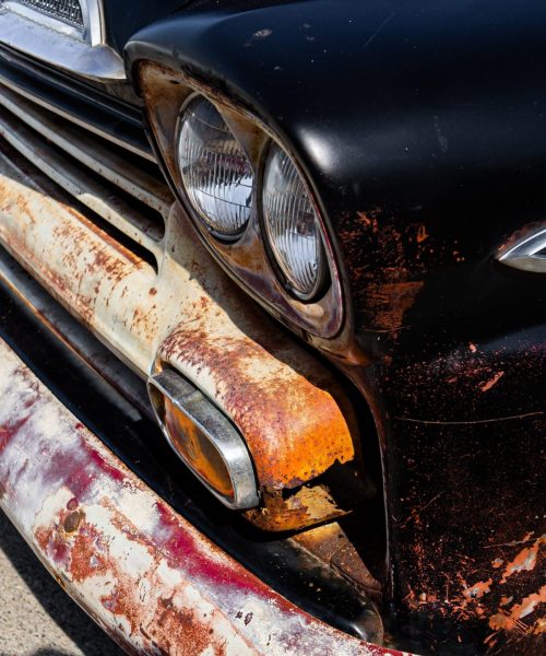 Vertical shot of the headlights and the bumper of an old rusty black automobile A vertical shot of the headlights and the bumper of an old rusty black automobile