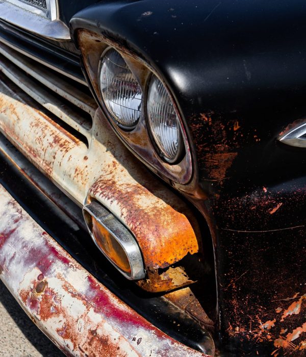 A vertical shot of the headlights and the bumper of an old rusty black automobile